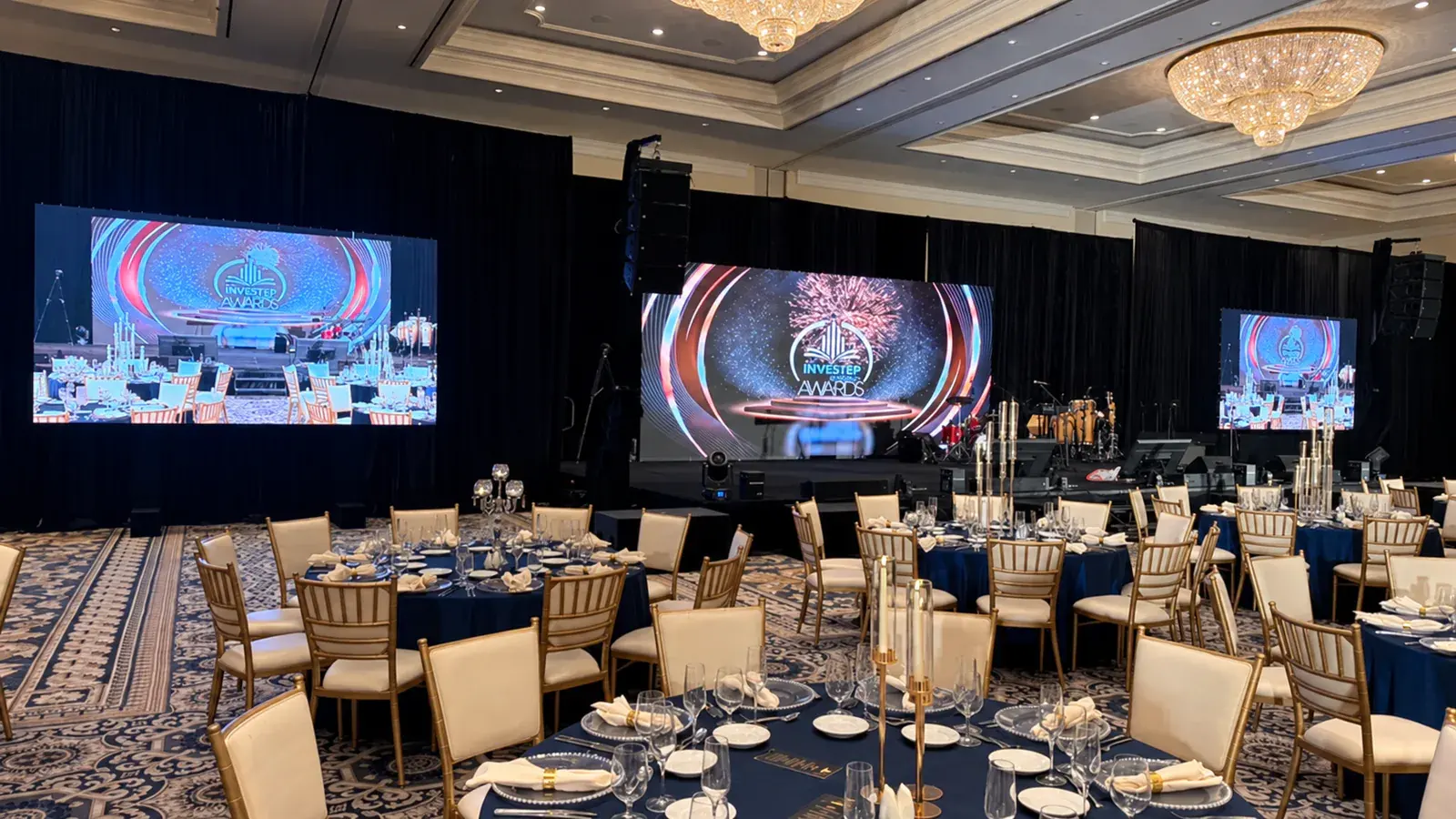 Awards gala ballroom with a lit stage, presentation screens and banquet tables
