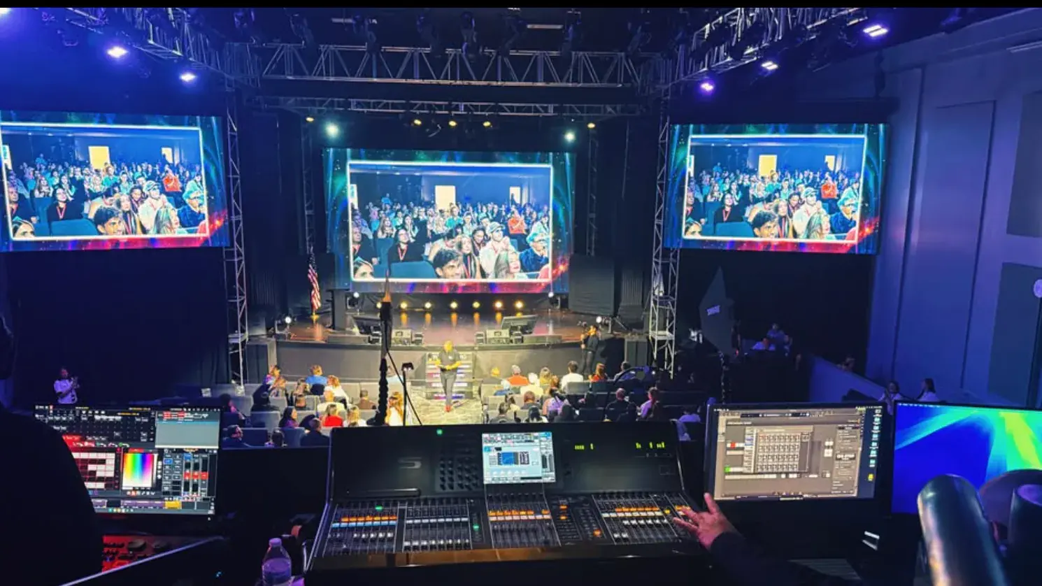 Audio and playback operators coordinating three event displays from the back of a theater