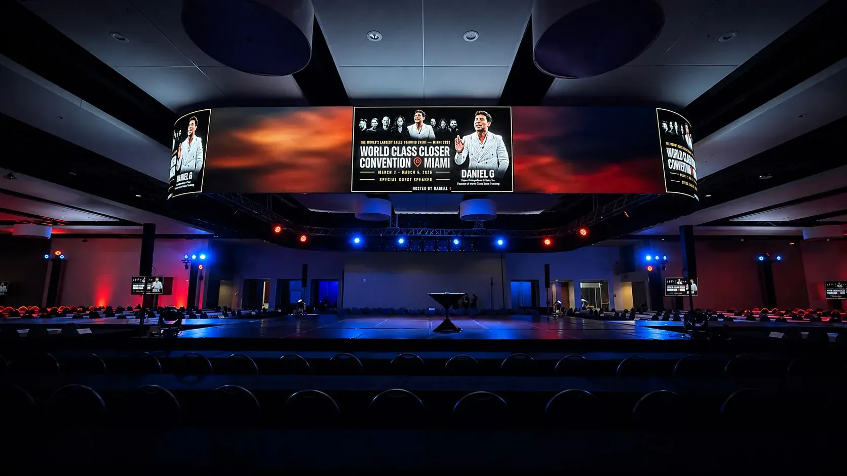 Conference room prepared with a central stage, suspended LED screens and red-blue lighting