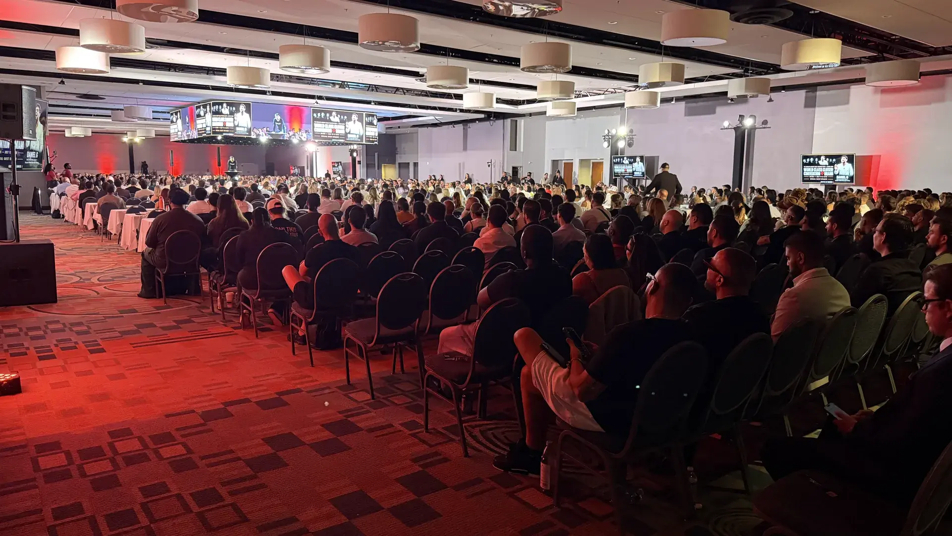 Wide view of the audience, central stage, event lighting, and video displays at a motivational conference in Miami