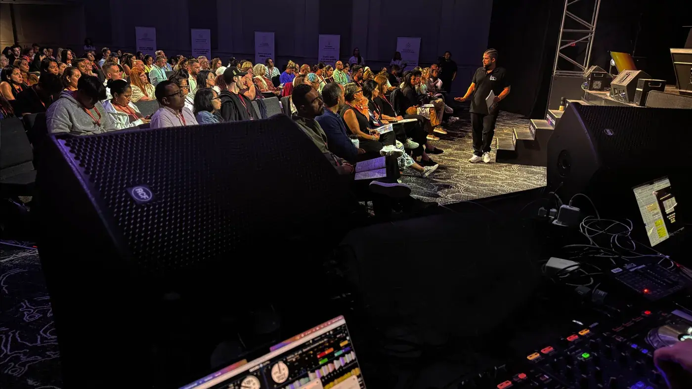 Audiencia de conferencia escuchando al presentador con refuerzo y monitoreo de producción en el salón