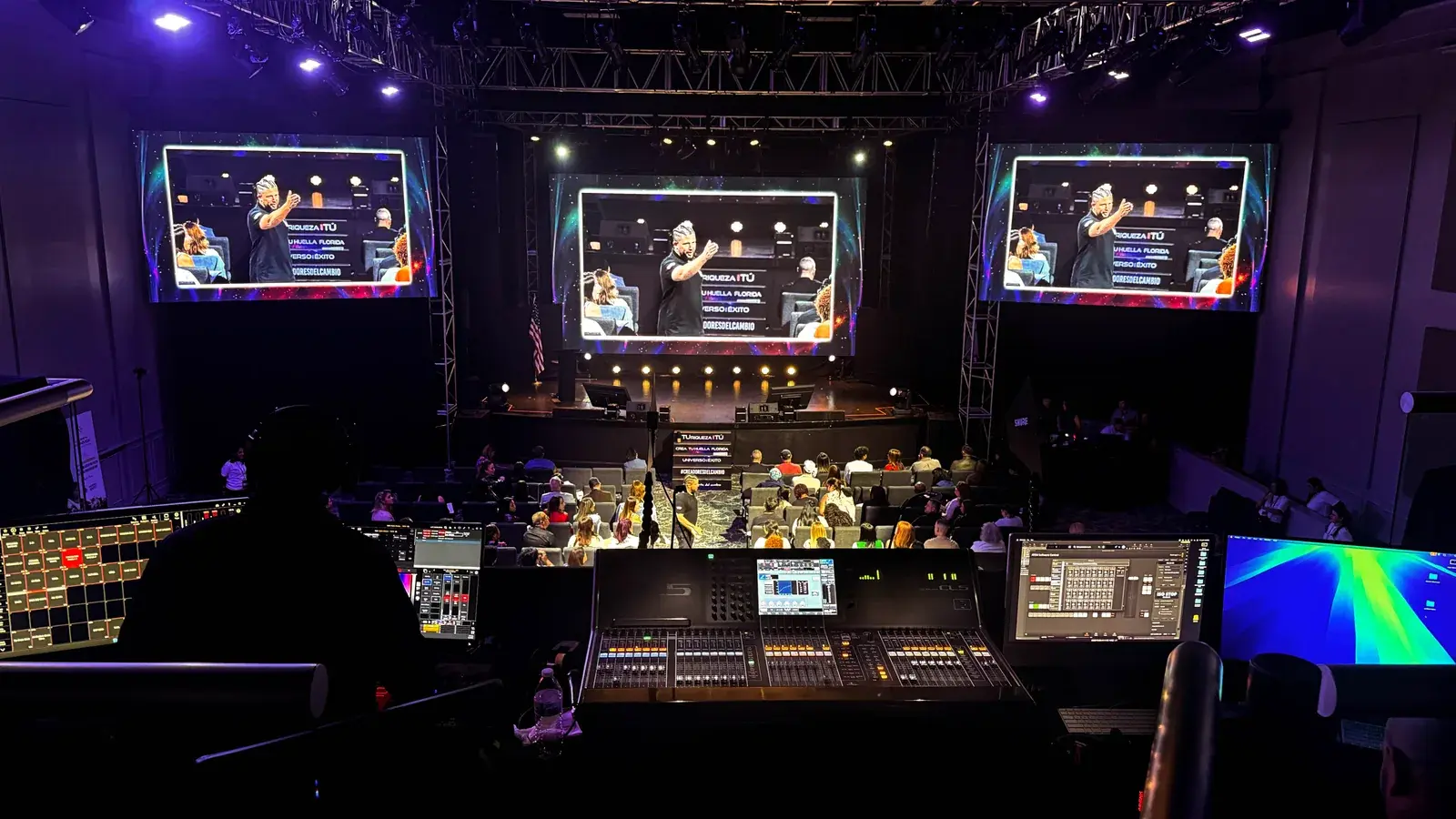 Escenario de conferencia con pantalla LED central, pantallas laterales, audiencia y posición de control de producción
