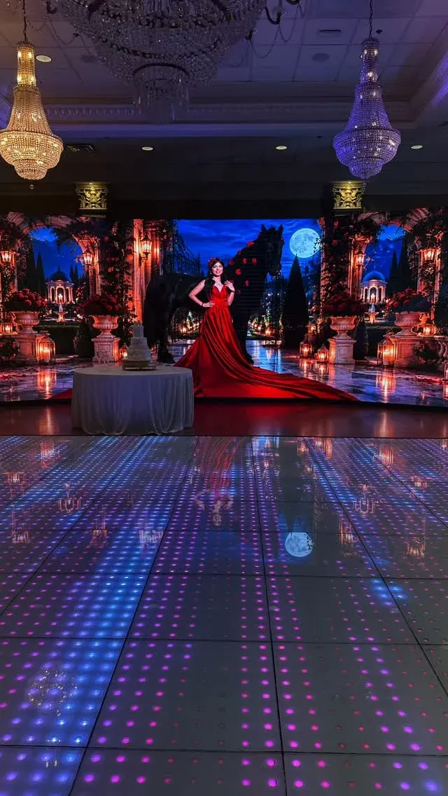 Quinceañera in a red gown beside an illuminated dance floor and themed LED backdrop